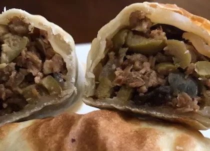 Close-up of a cut-open empanada, revealing a filling of meat and olives, golden crust visible.