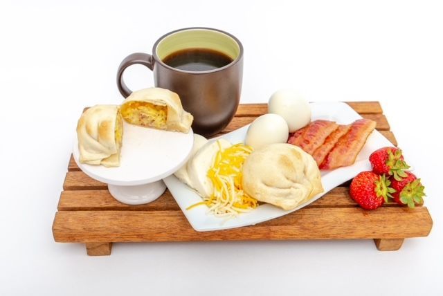 Breakfast tray: coffee, empanada, eggs, bacon, cheese, strawberries on a wooden board.