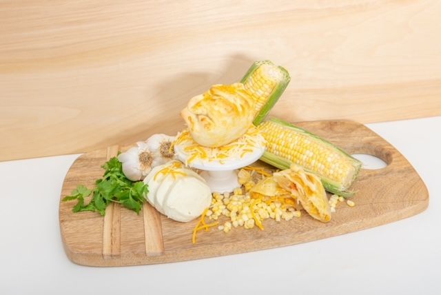 Corn, cheese, garlic, and herbs on a wooden cutting board.