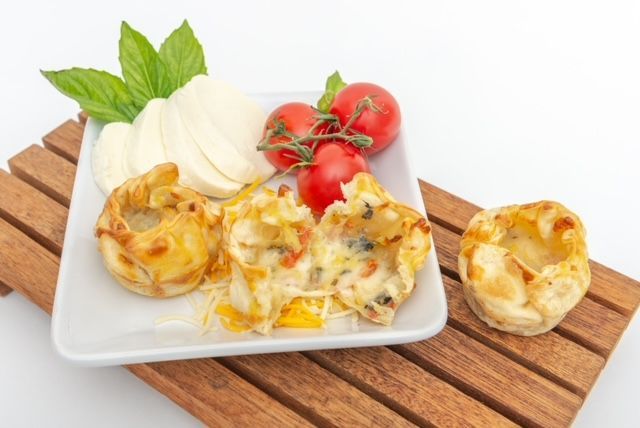 Appetizer dish with baked pastry cups, mozzarella, tomatoes, and basil on a wooden surface.