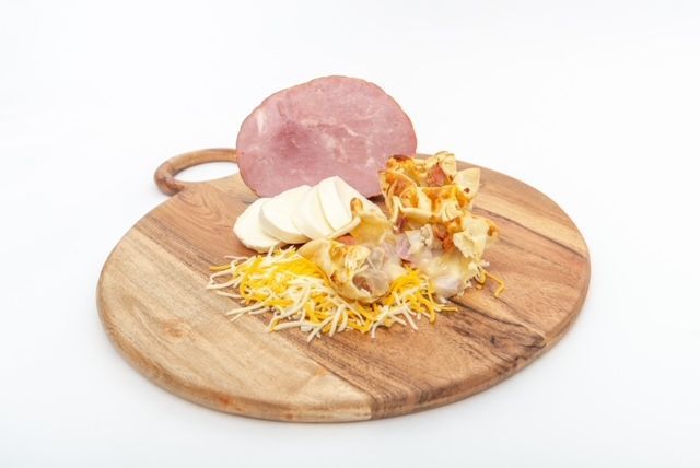 Ham, cheese, and egg casserole with ham and cheese on a wooden cutting board.