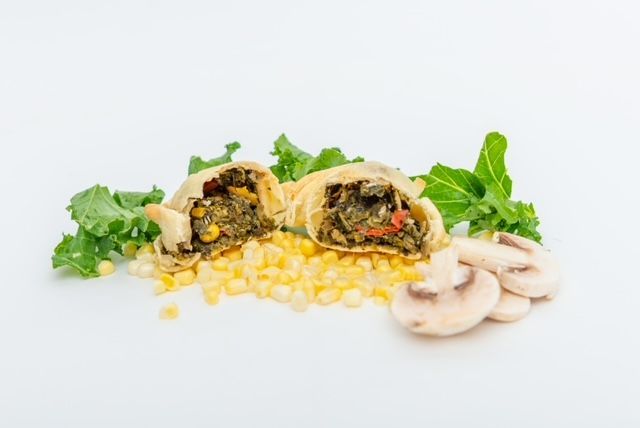 Savory hand pie cut in half, filled with vegetables, surrounded by corn, mushrooms, and greens.