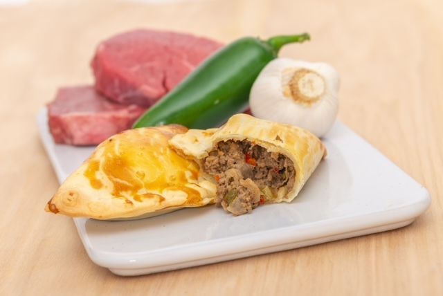 Empanada with a meat filling, surrounded by steak, jalapeno, and a mushroom on a white plate.