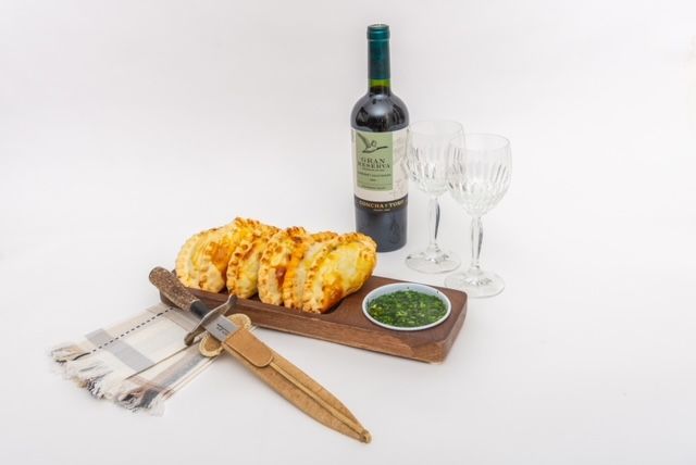 Bread, wine, and dipping sauce with glasses, on a wooden serving board with a knife and cloth.