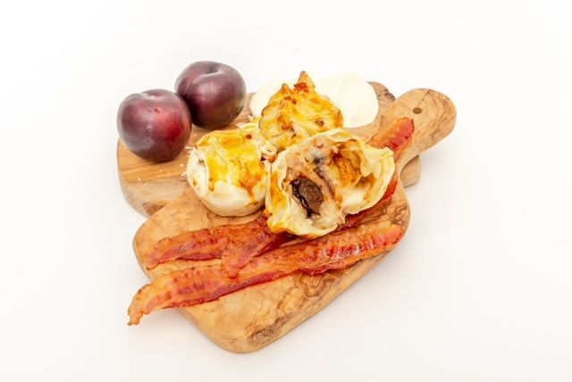 Wooden board with plums, muffins, bacon, and cream.