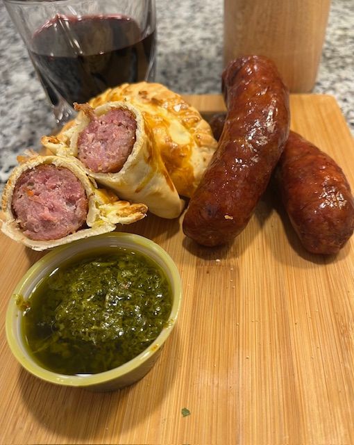 Sausage, chimichurri, and empanadas on a wooden board with red wine.