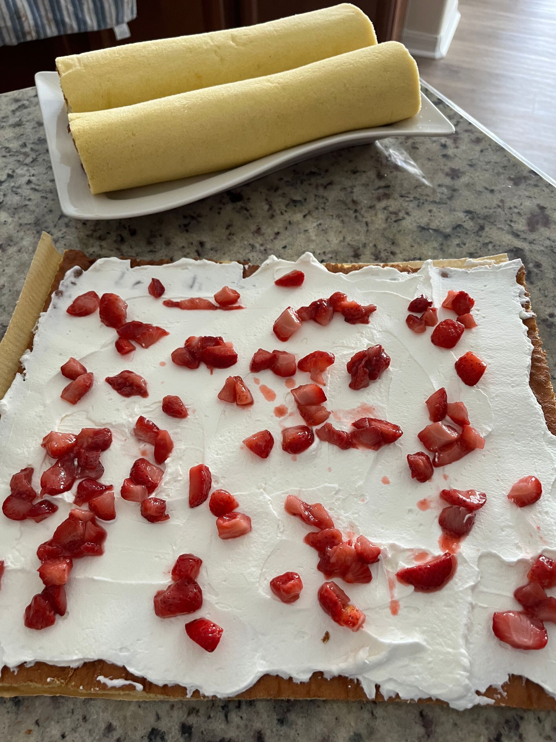 Cake roll assembly: sponge cake with whipped cream and chopped strawberries.