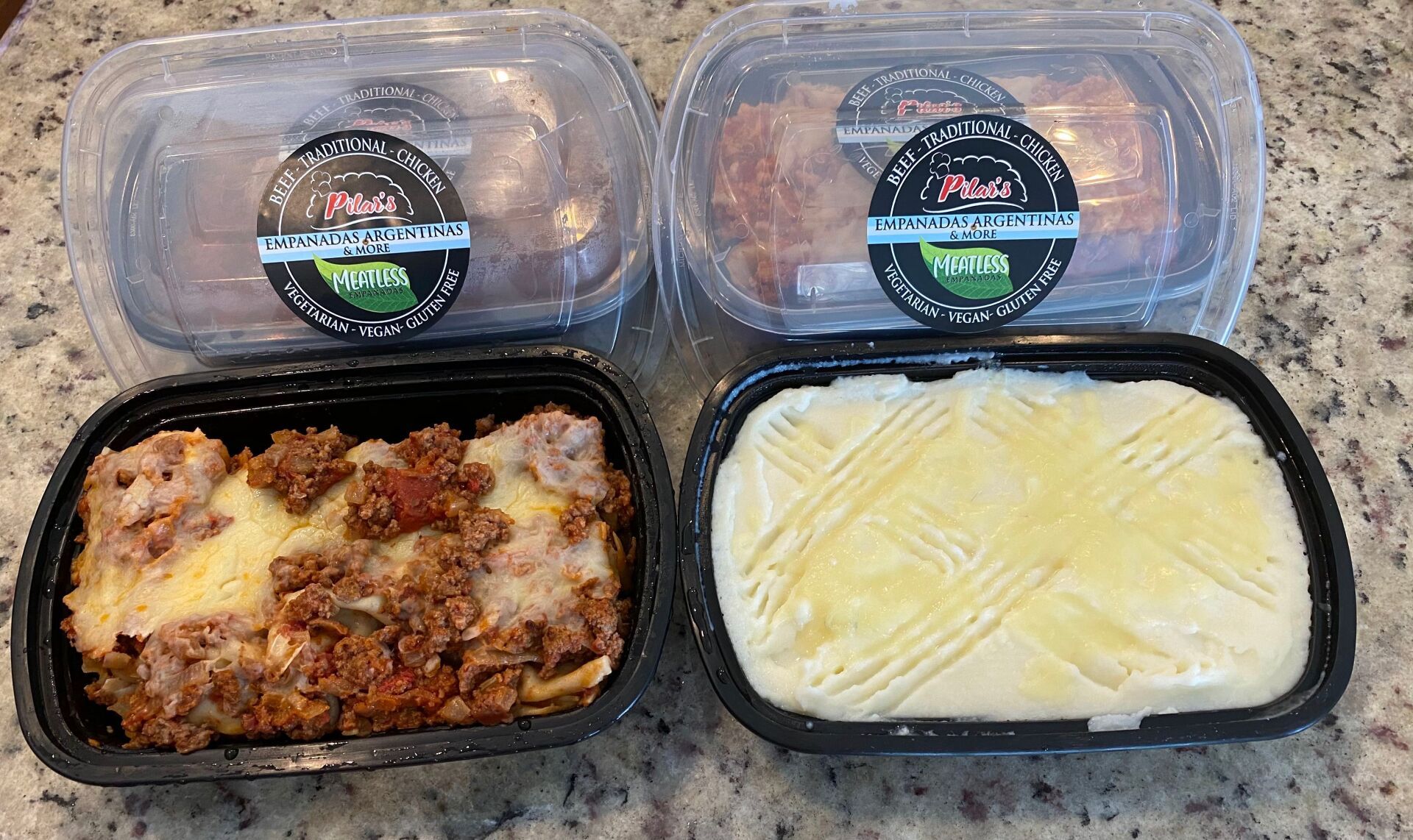 Four takeout containers of prepared food: lasagna, mashed potatoes, and two meat dishes.