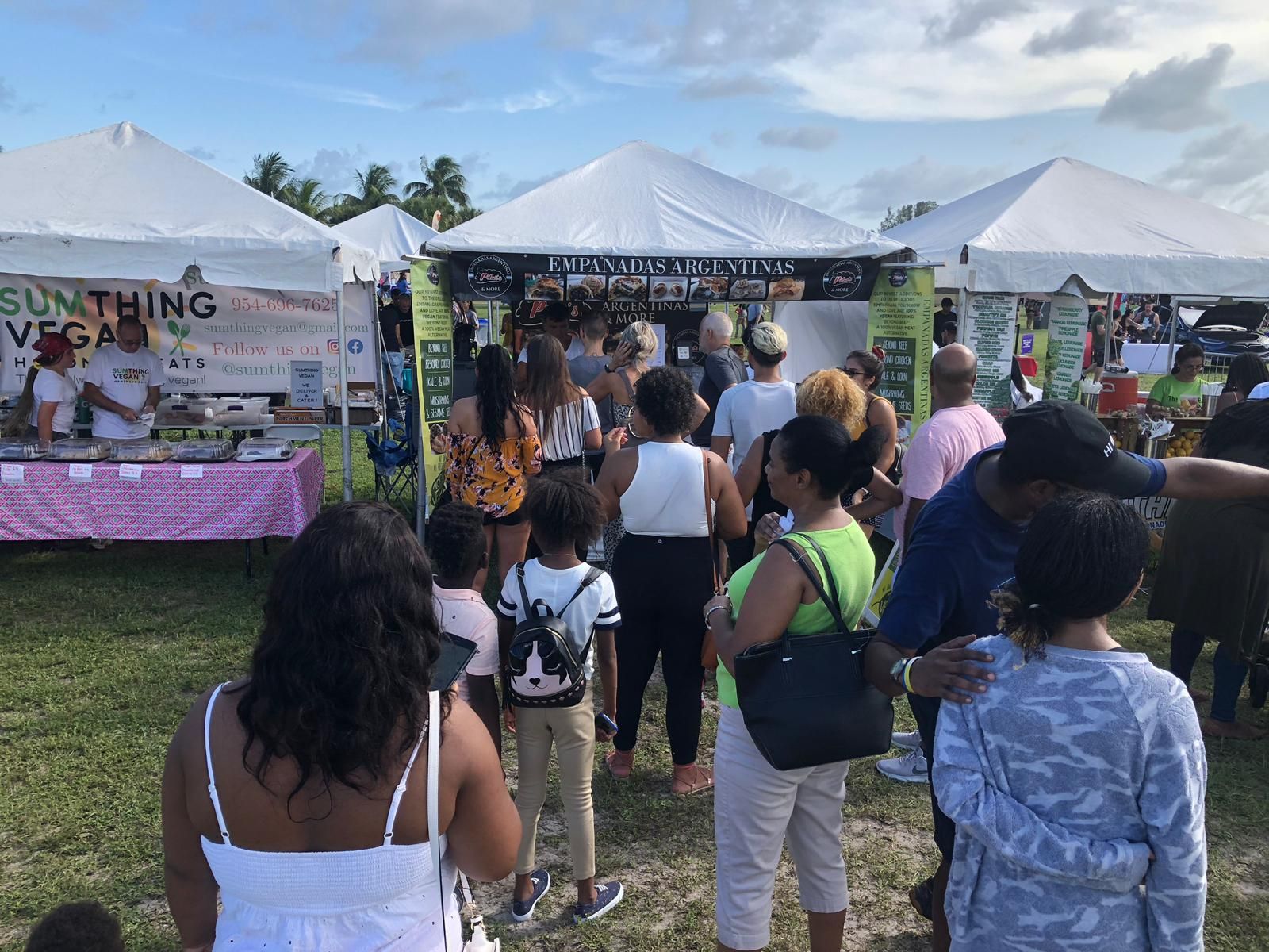 People at a food market with tents, many are looking at a vendor in the center.