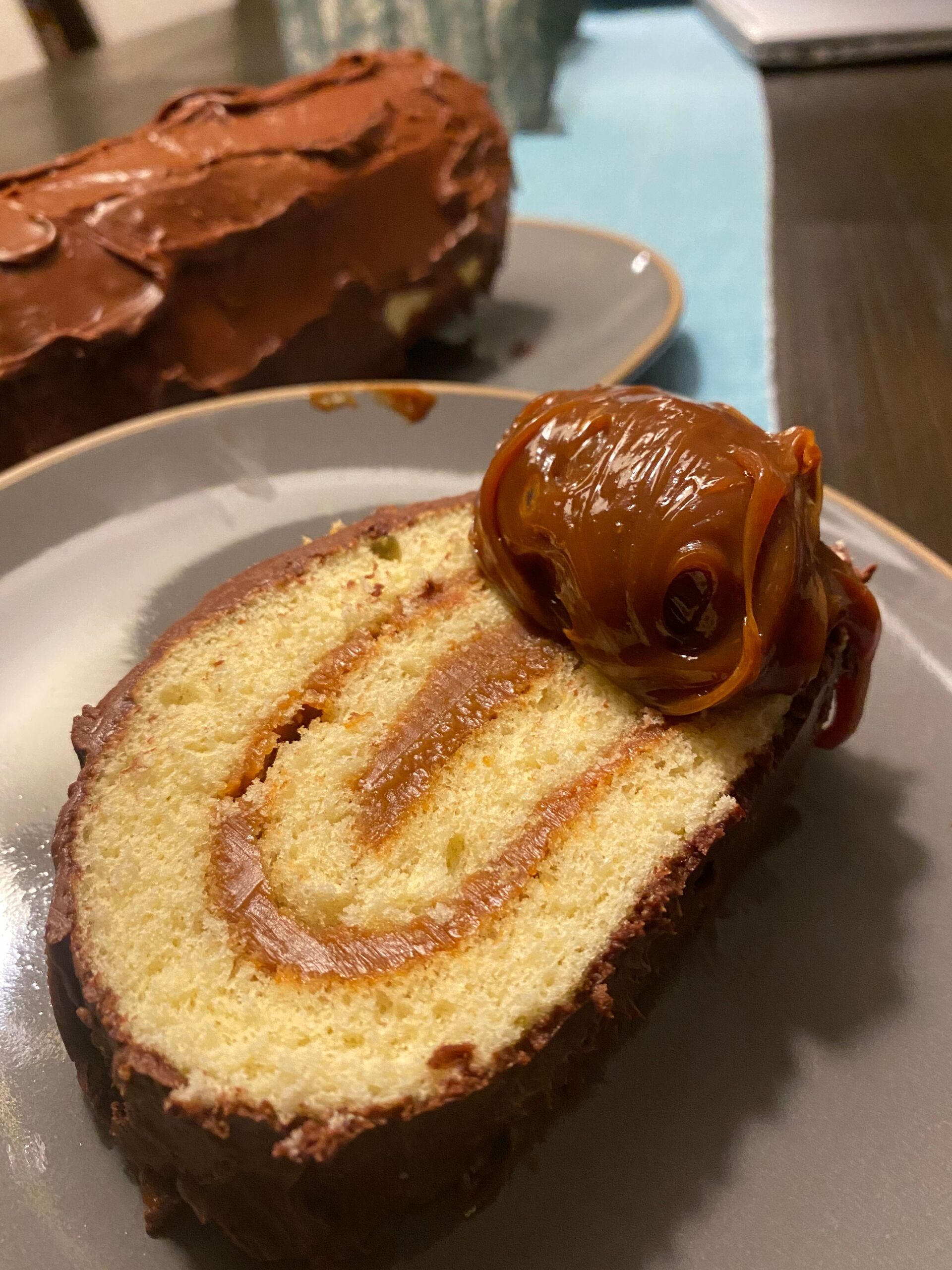 Slice of cake roll with caramel topping, chocolate frosting, and spiral filling.
