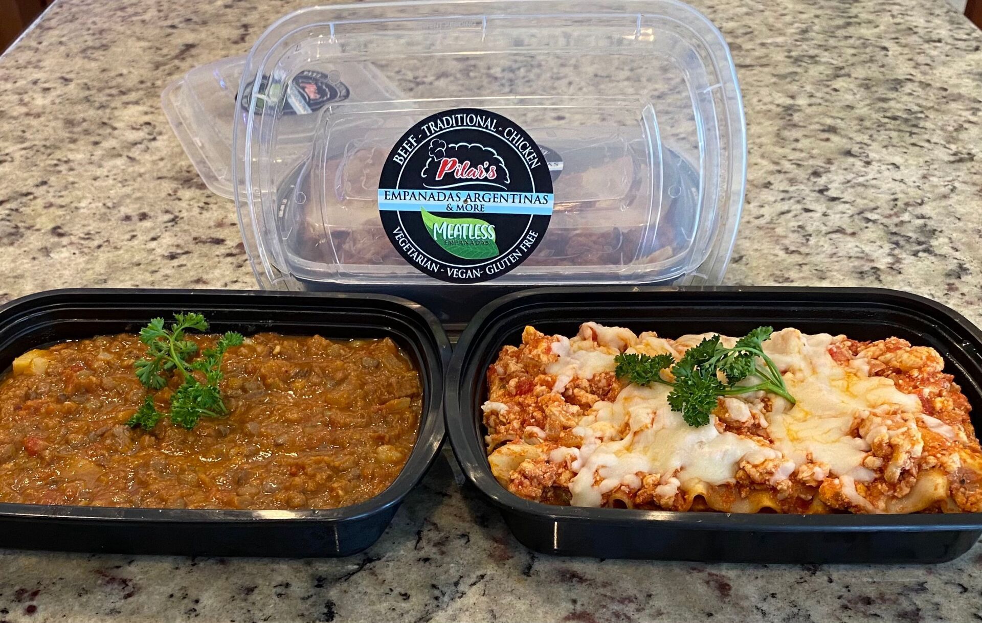 Two pasta dishes and a bread container on a countertop.