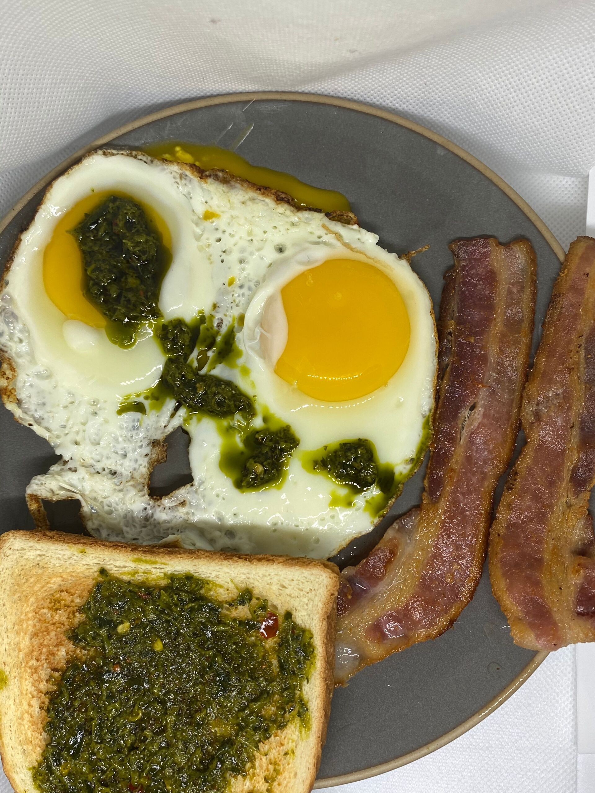 Fried eggs and bacon with pesto and toast on a gray plate.