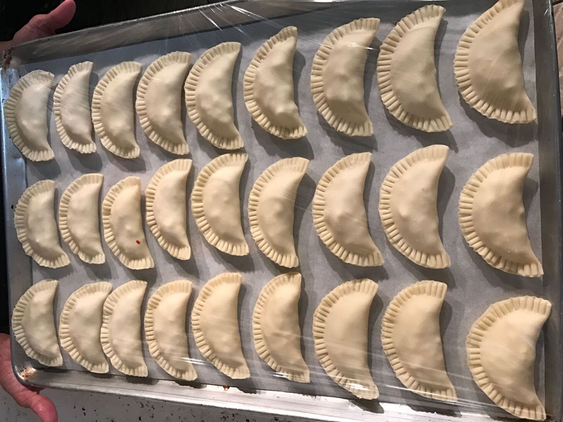 Tray of uncooked, crimped pastries on parchment paper.