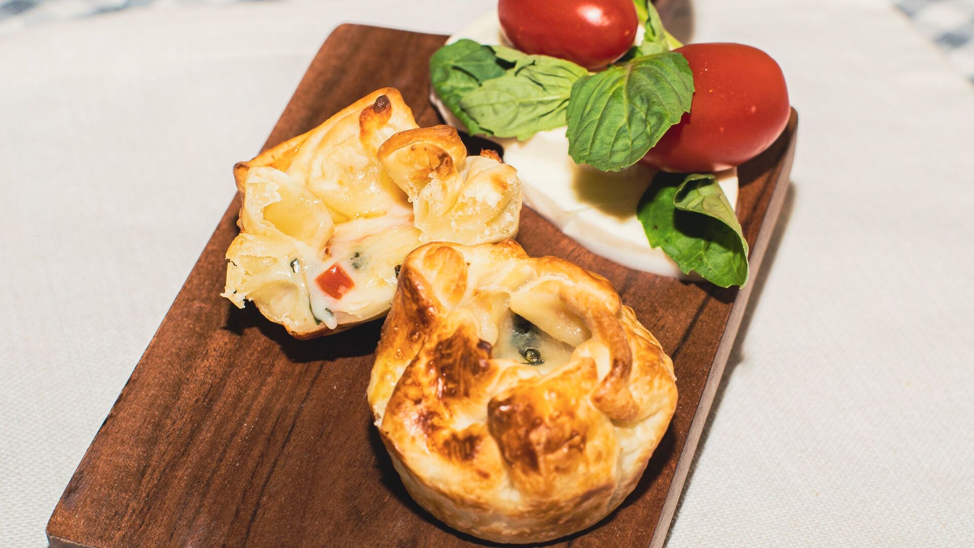 Appetizer on wooden board: pastries, mozzarella, cherry tomatoes, and basil.