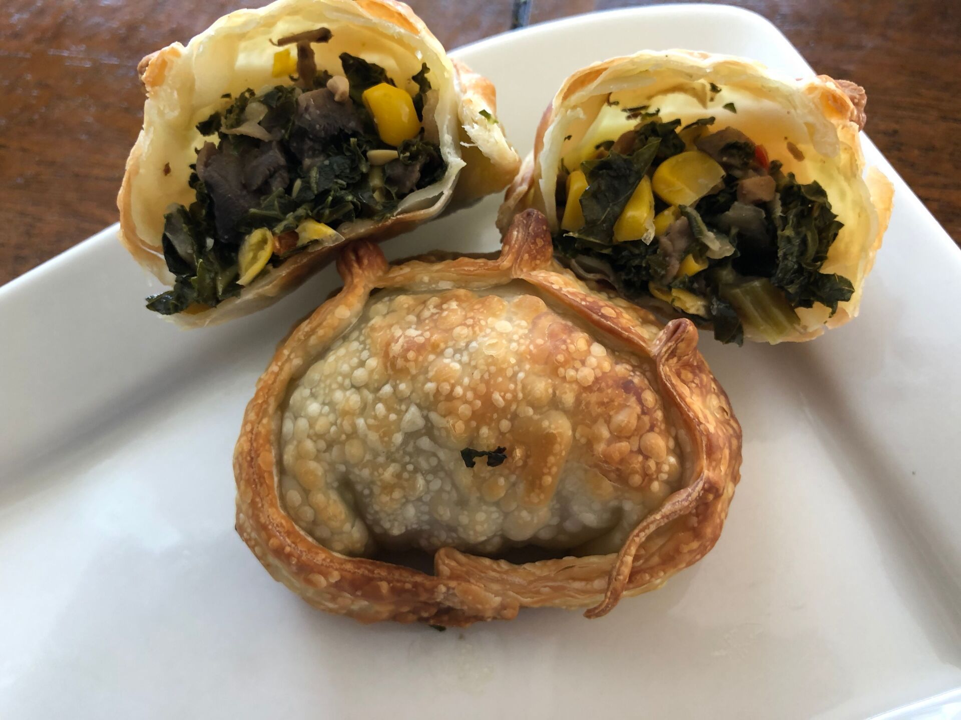 Fried empanada cut open, revealing filling of spinach, corn, and mushrooms on white plate.