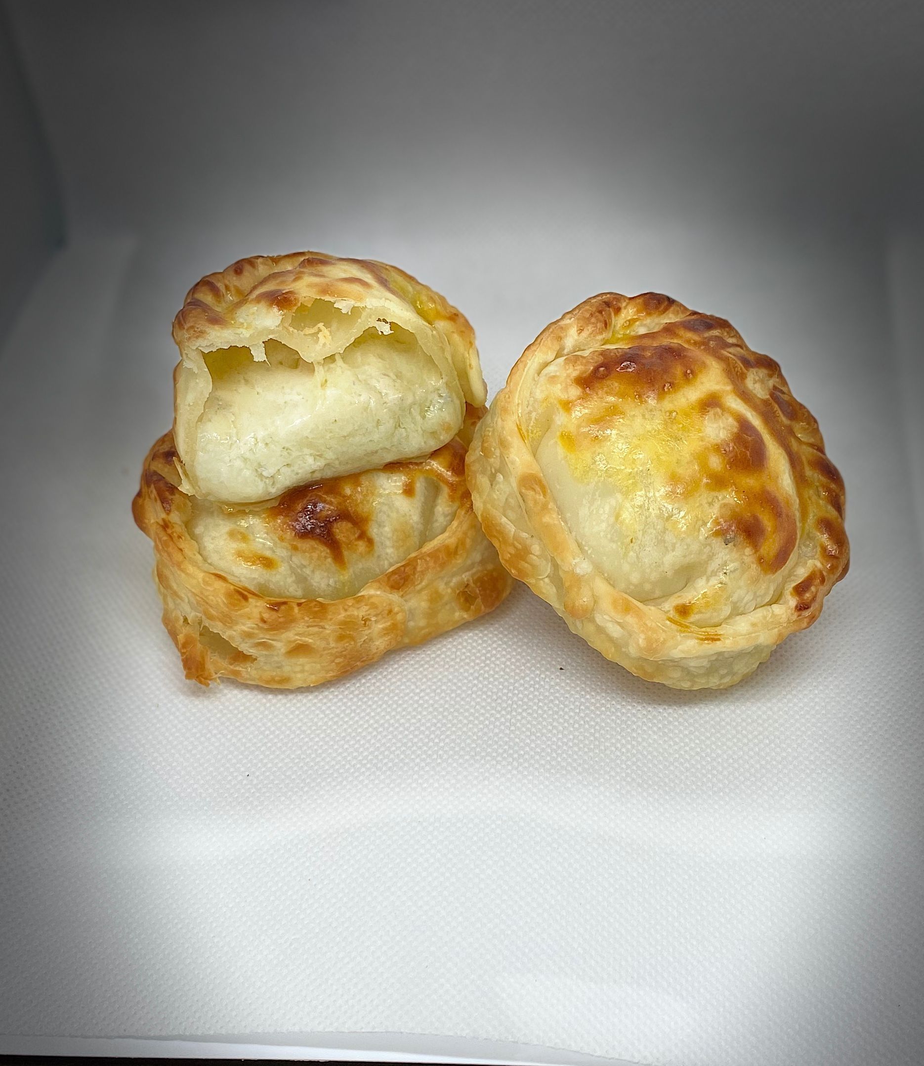 Three baked pastries on white cloth, golden-brown and round. One is stacked on top.