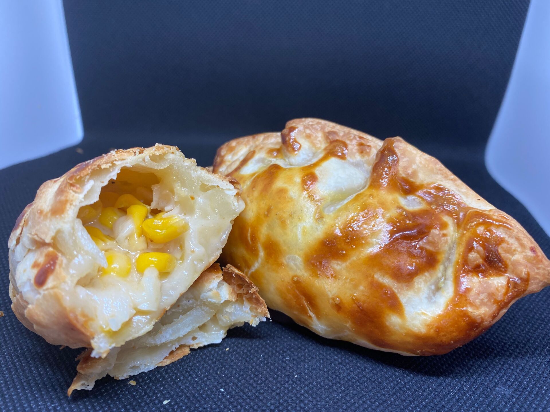 Golden baked empanada, split open to show corn and potato filling.