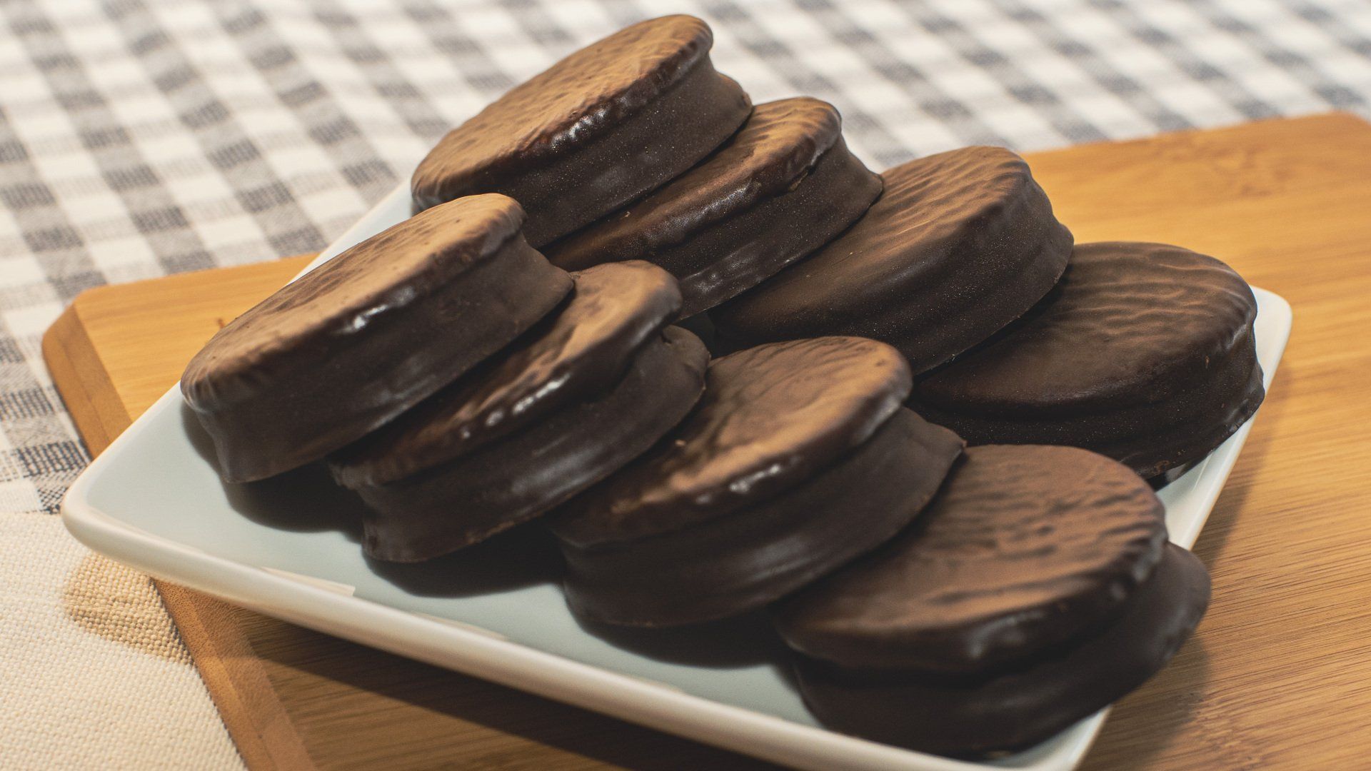 Chocolate alfajores stacked on a white plate, wooden background.
