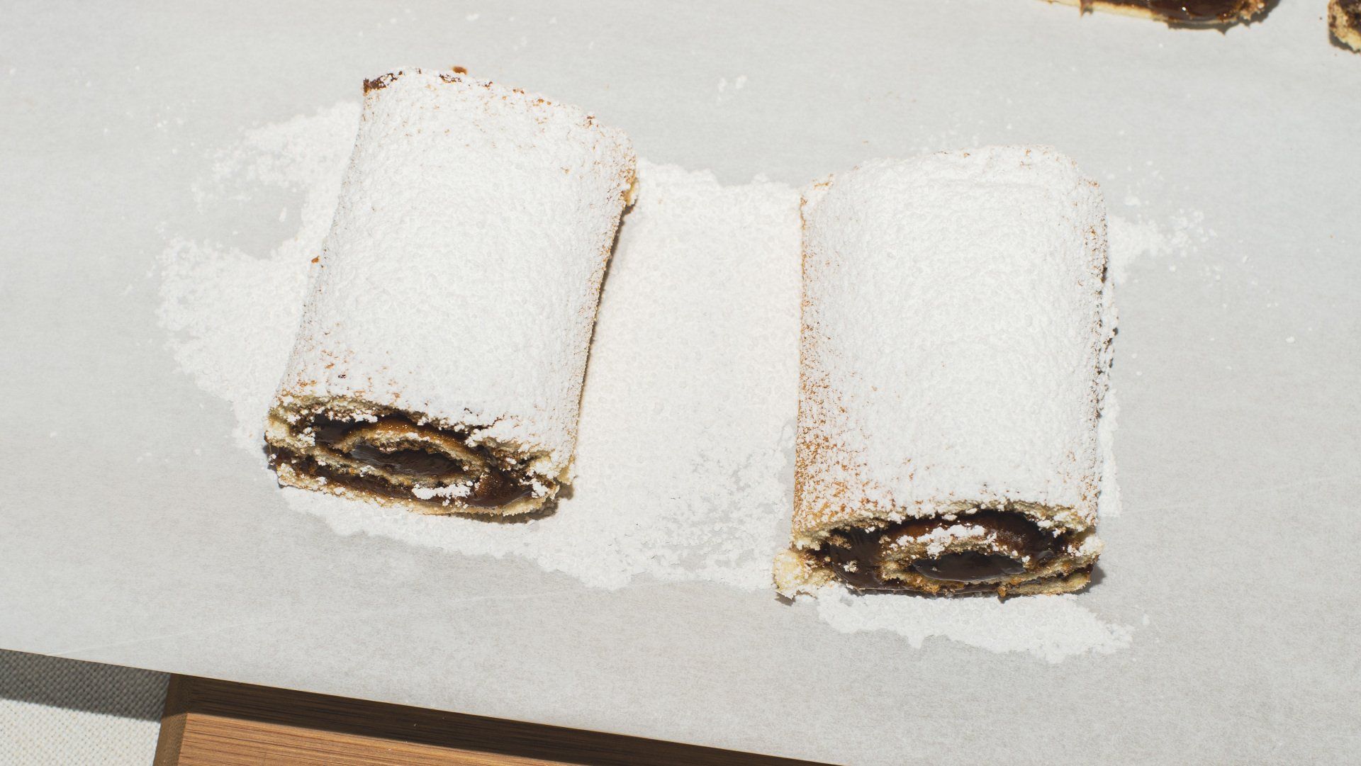 Two pastry rolls dusted with powdered sugar on a white surface.