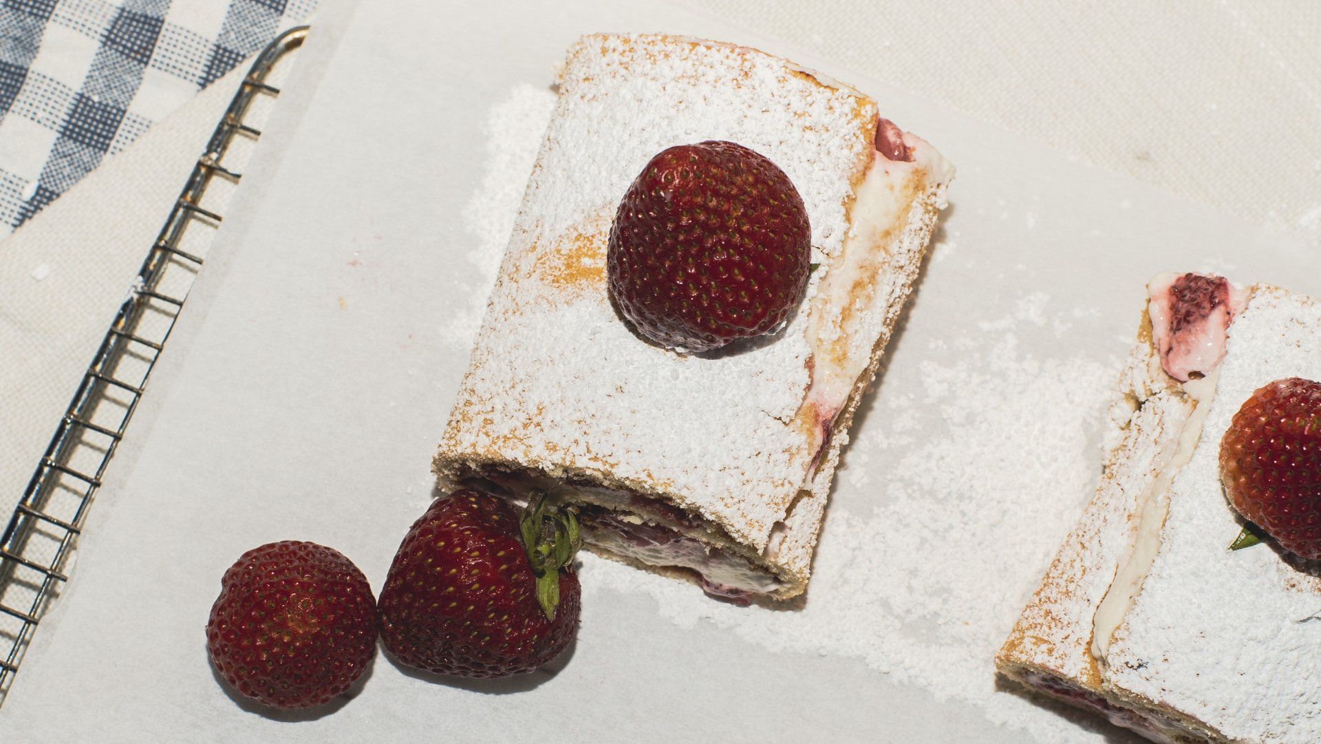 Strawberry pastry dusted with powdered sugar, served with fresh strawberries on a white surface.