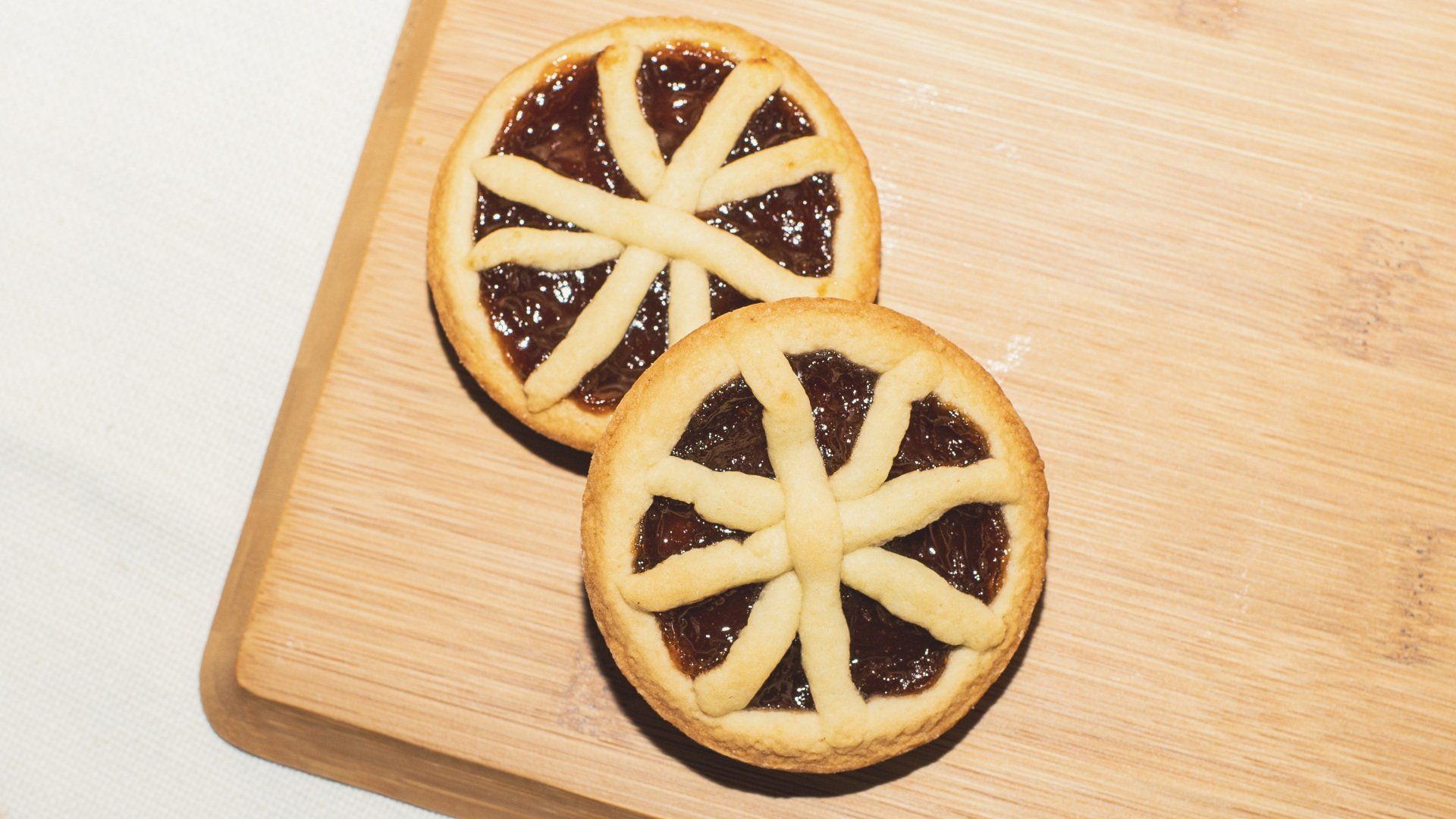Two small tarts with jam filling and lattice pastry crusts on a wooden board.