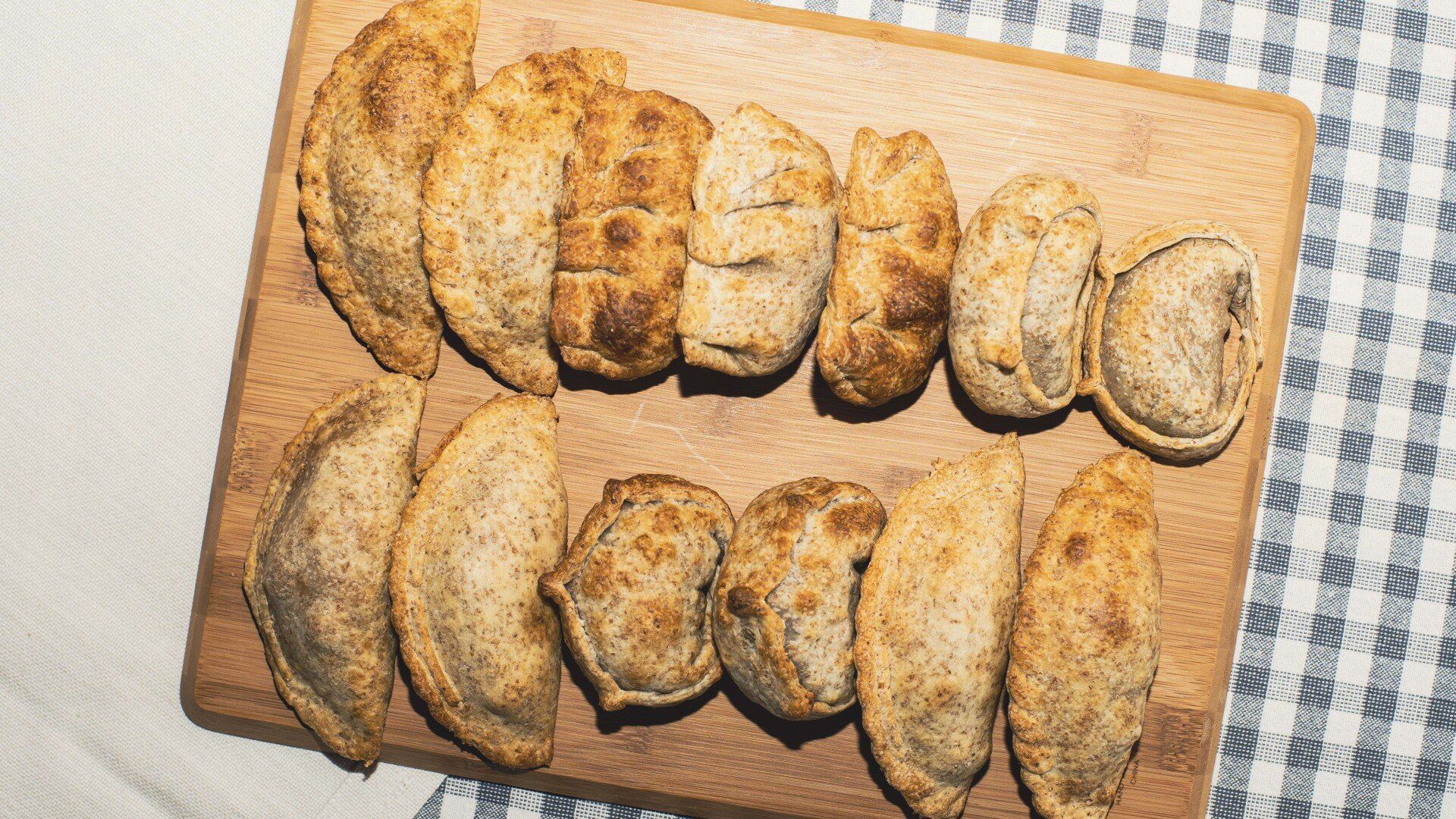 Golden-brown savory pastries on a wooden board, resting on a checkered tablecloth.