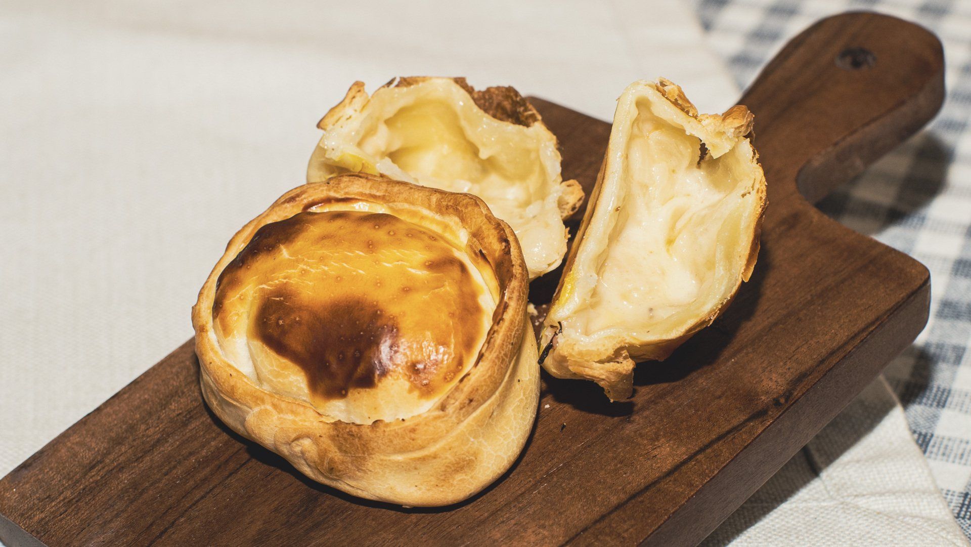 Pasties on a wooden board, with golden-brown crusts and visible creamy filling.