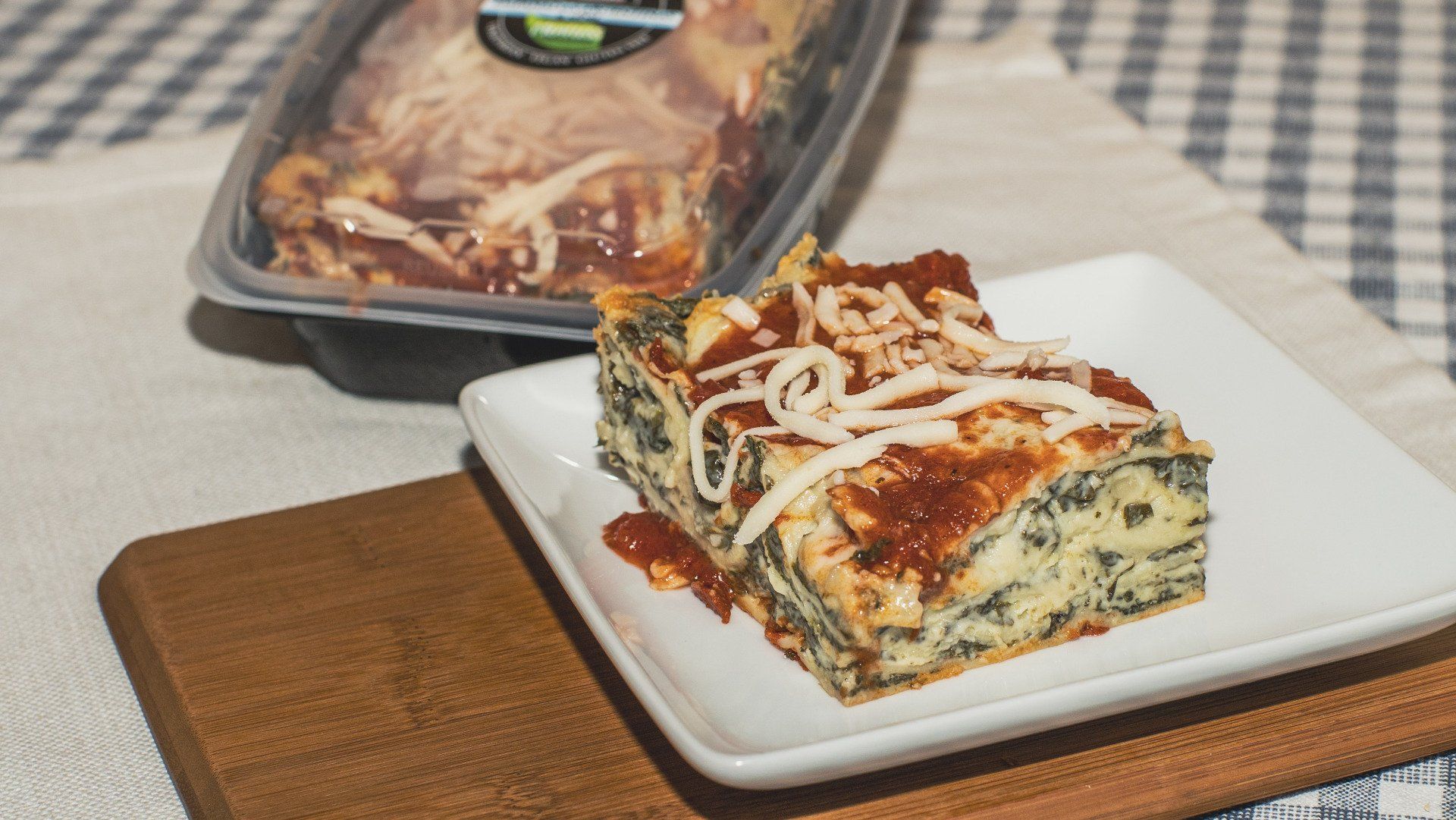 Lasagna on a square white plate with a package of lasagna in the background.