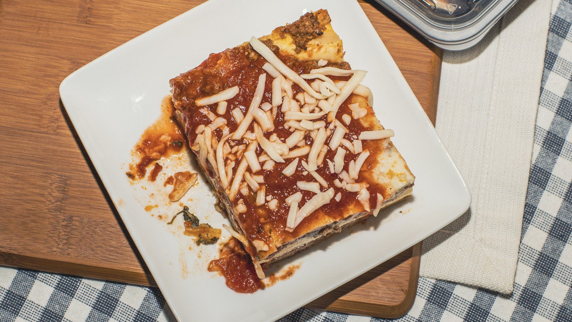Slice of lasagna on white plate, topped with sauce and cheese.