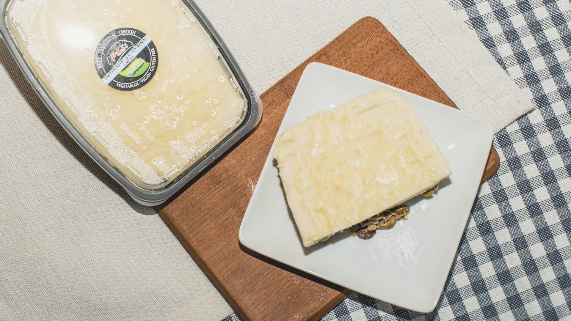 Cheese, packaged and sliced, on a wooden board and white plate, checkered table.