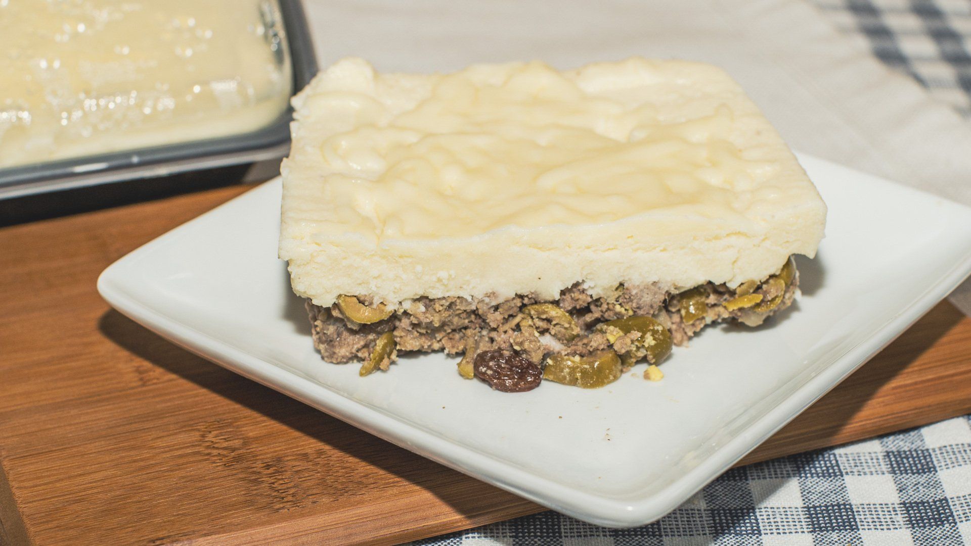 A square slice of savory meat pie with pale crust on a white plate.