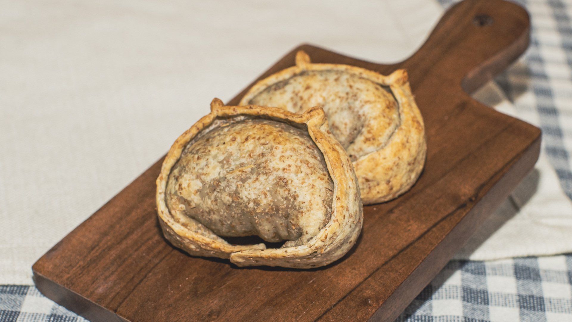 Two savory empanadas on a wooden board over a checkered tablecloth.