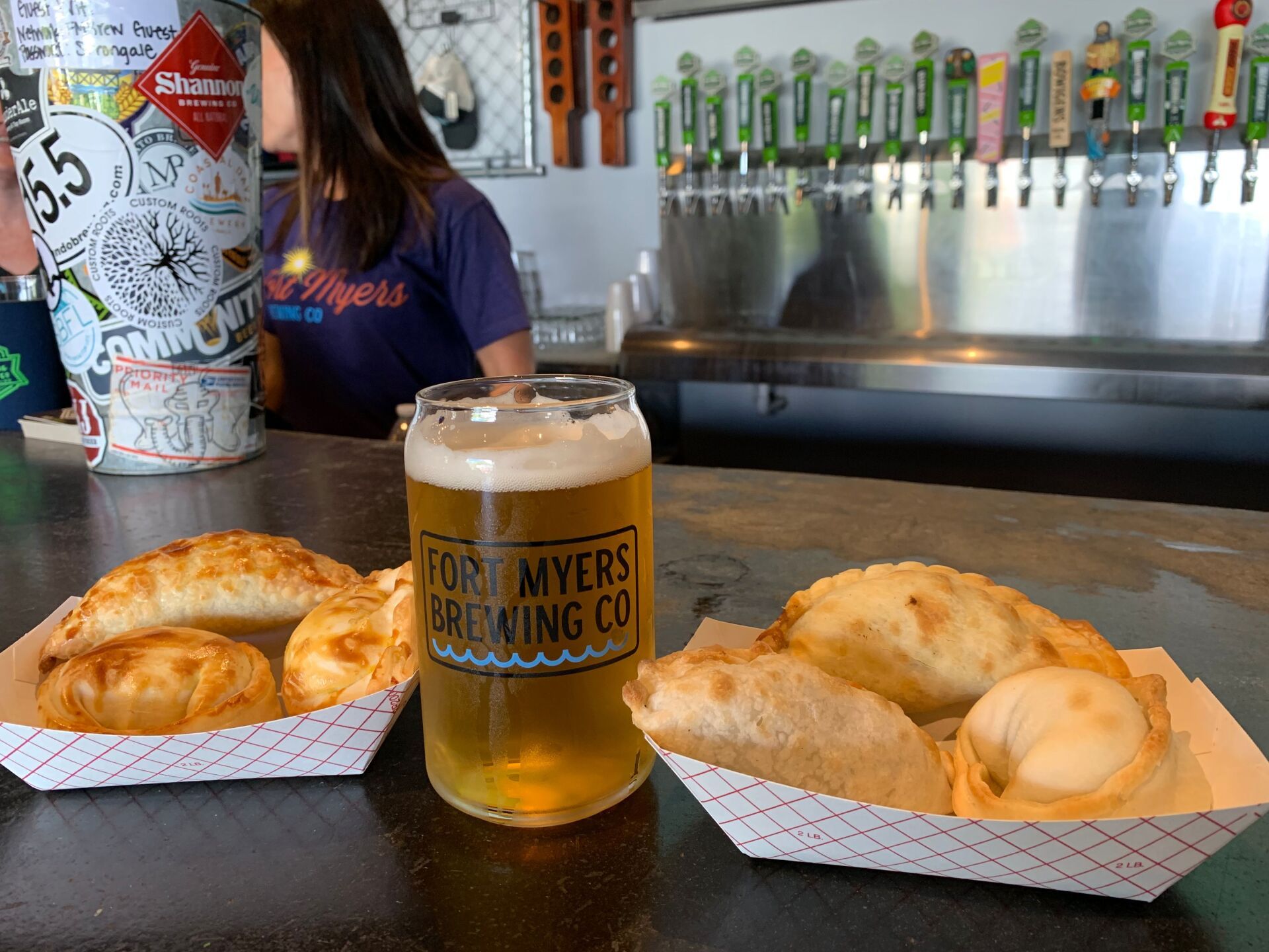 A beer and empanadas on a bar; a person is in the background at Fort Myers Brewing Co.