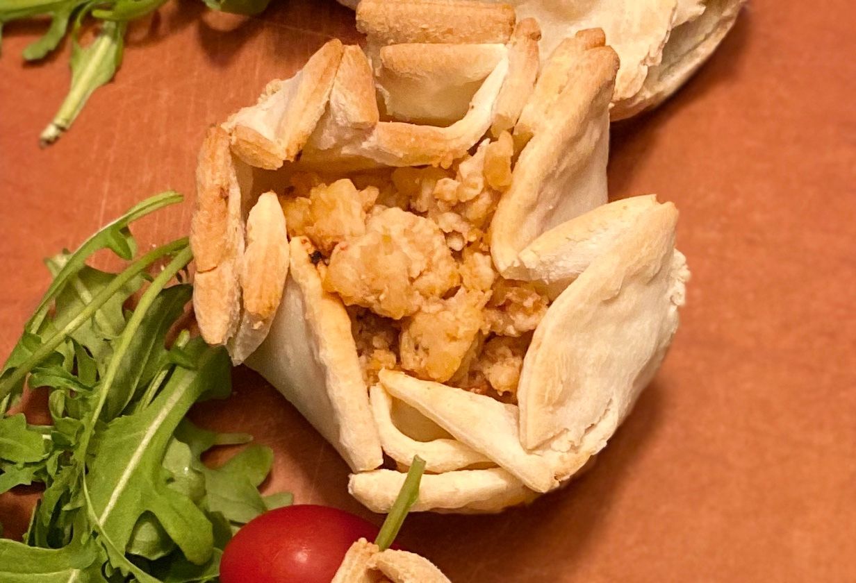 Chicken filling in a pastry cup with arugula and a cherry tomato on a wooden surface.