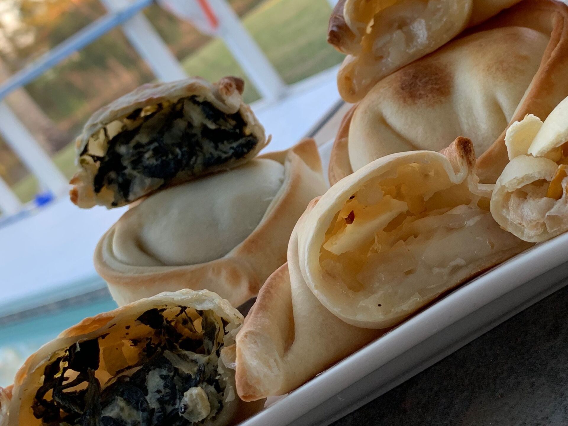 Plate of baked empanadas, some cut open, revealing spinach and cheese fillings.