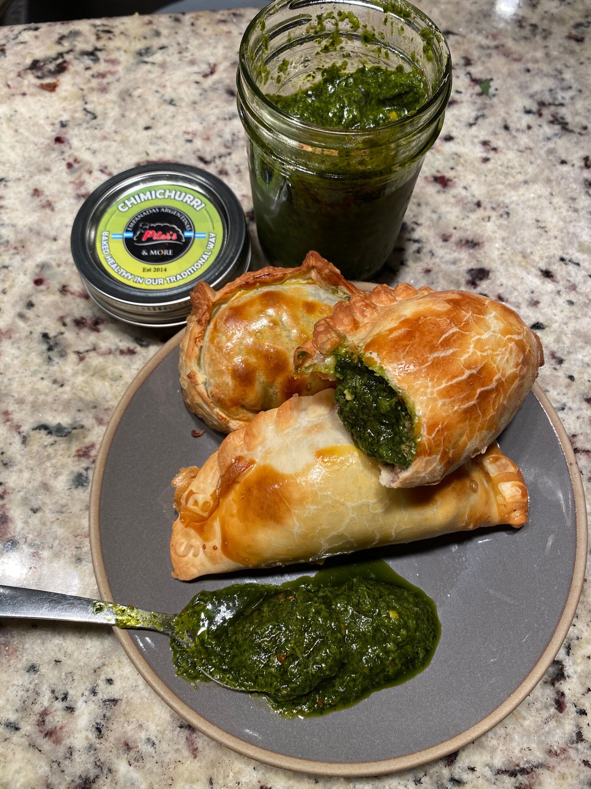 Empanadas with a vibrant green chimichurri sauce, and jar of sauce.