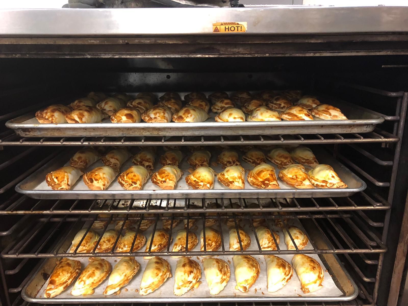 Empanadas baking in an oven on multiple racks, golden brown pastries.