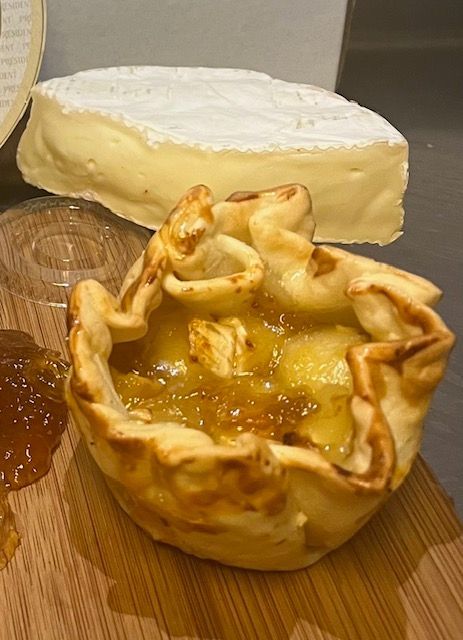 Baked brie pastry with a slice of brie cheese and jam on a wooden board.