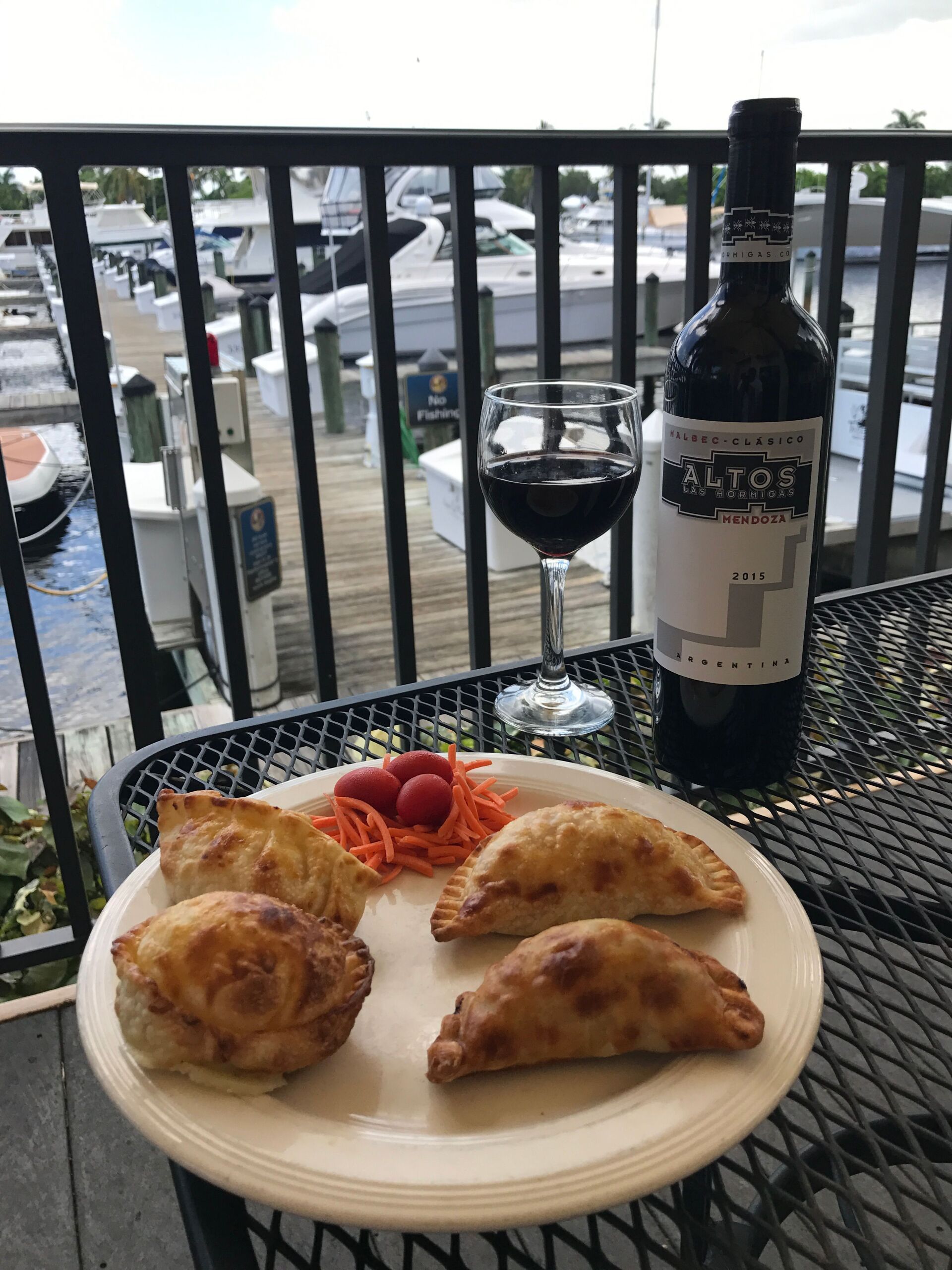 Plate of empanadas, wine, and bottle on a table overlooking a marina.