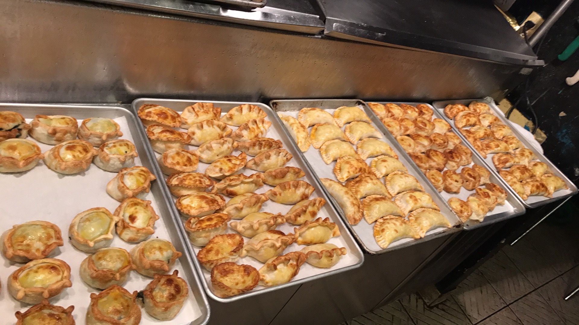 Several trays of baked savory pastries on a counter, ready to serve.