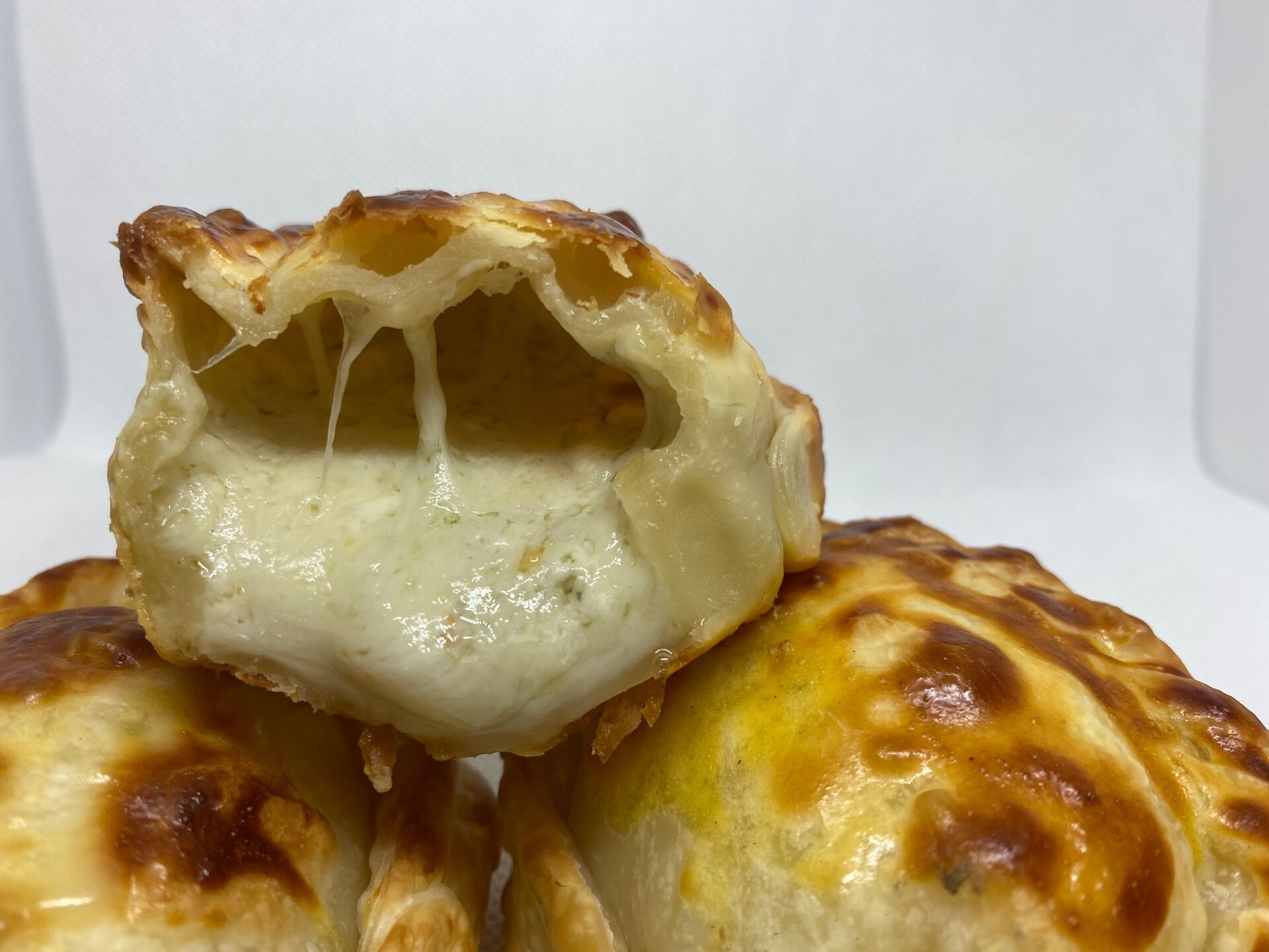 Close-up of an empanada cut open, showing melted cheese. Golden crust, white background.