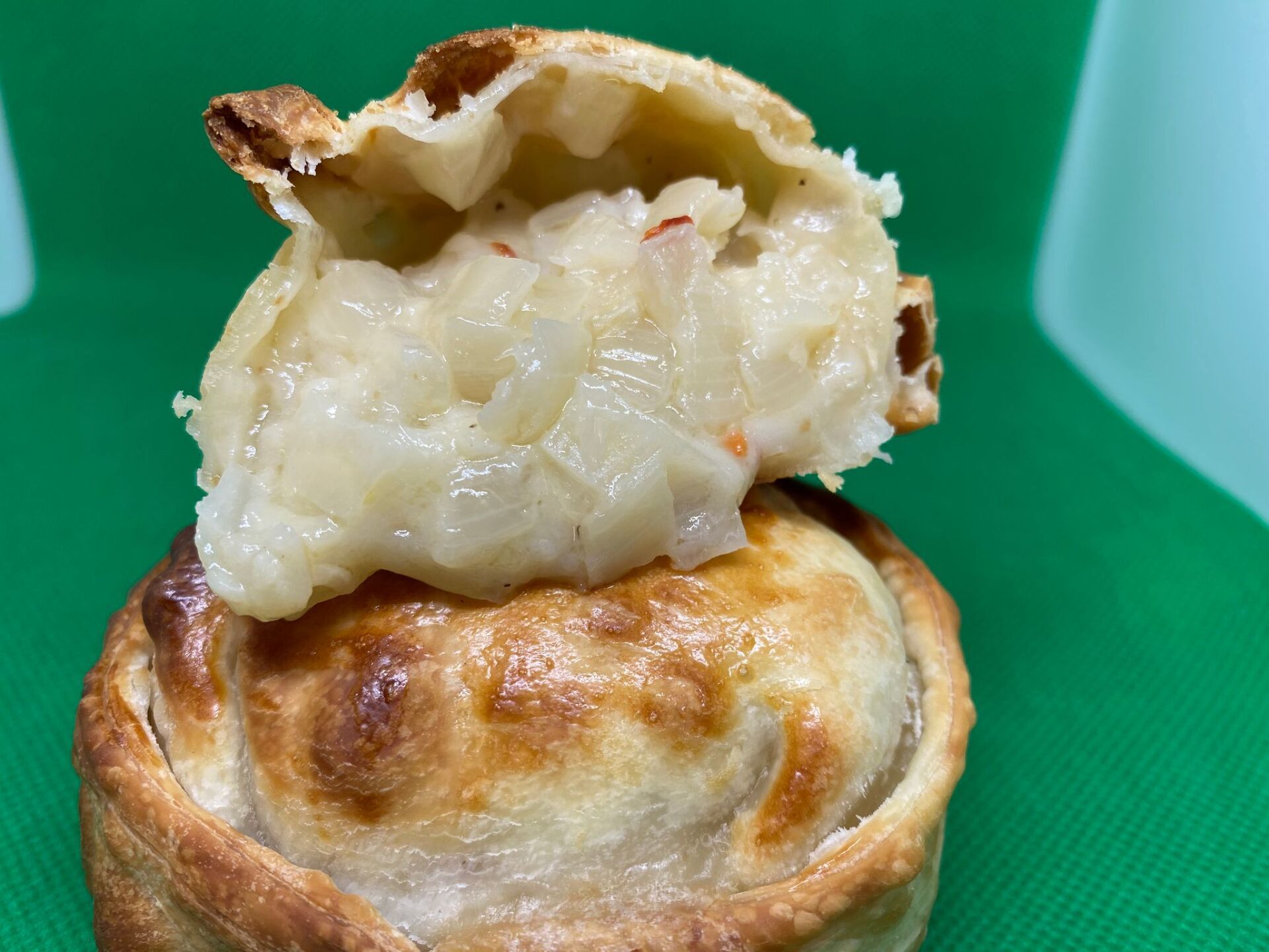 Golden-brown pastry empanada, top broken open, filled with creamy onion and pepper filling.