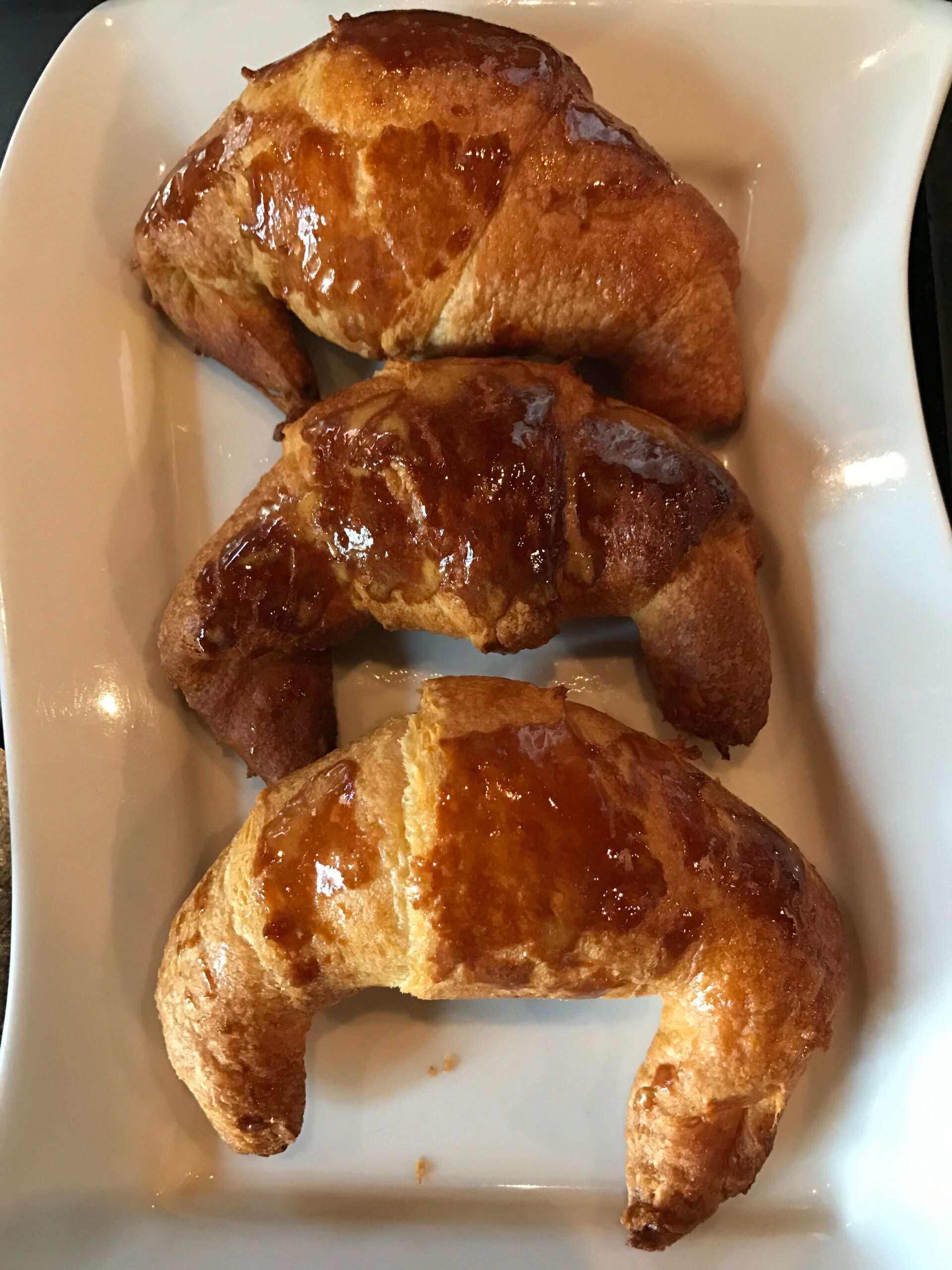 Three golden croissants arranged on a white rectangular plate.
