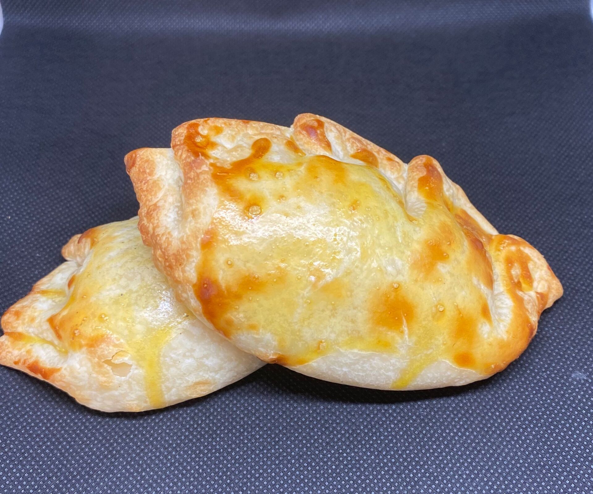 Two golden-brown empanadas on a dark background, ready to eat.