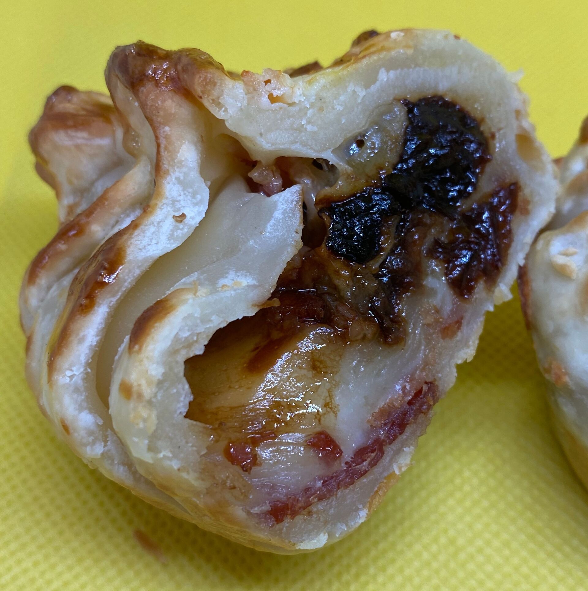 Pastry with filling, showing dark fruit, light cheese, and cooked meat on yellow background.