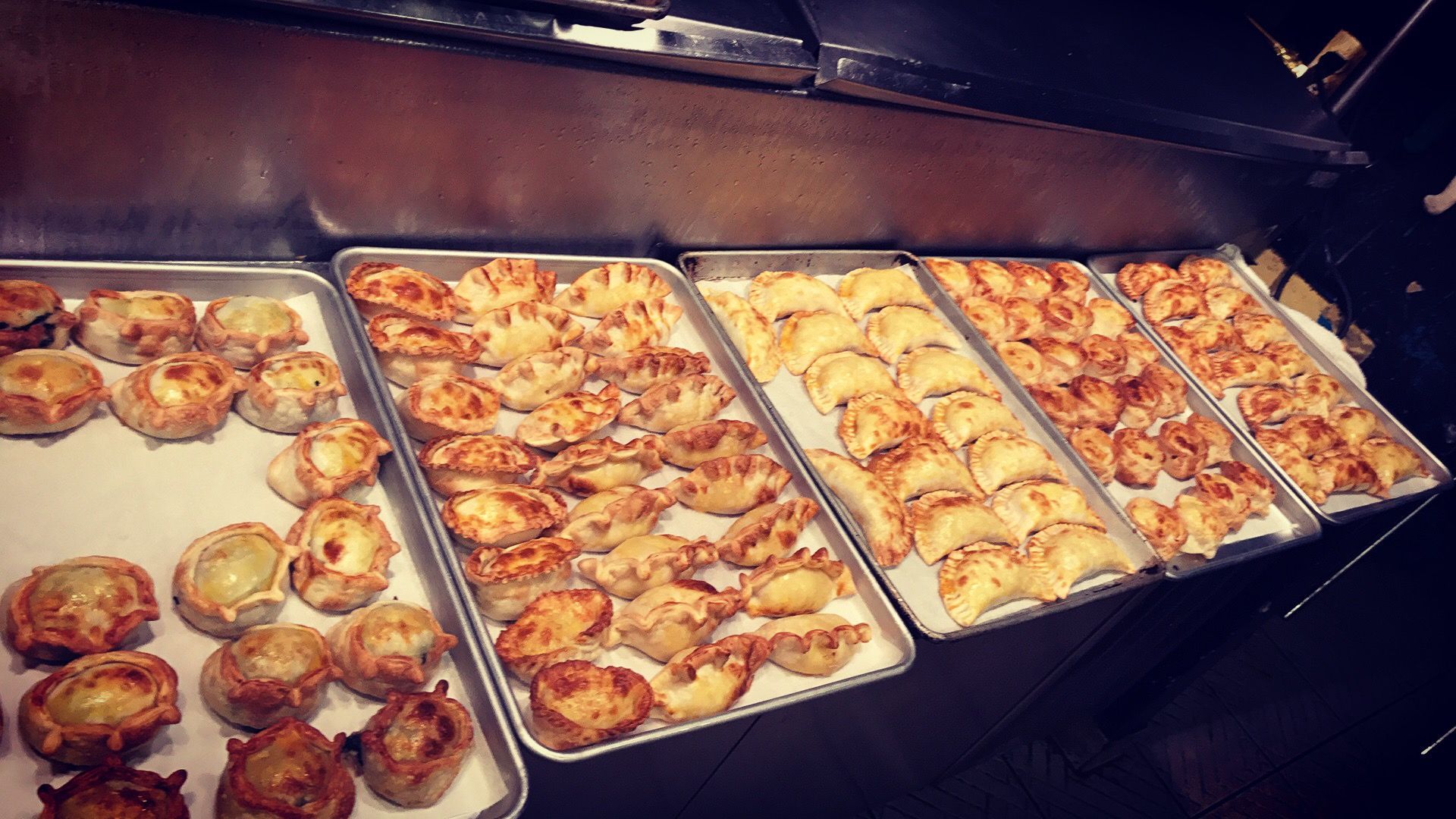 Baked pastries on metal trays under a shelf.