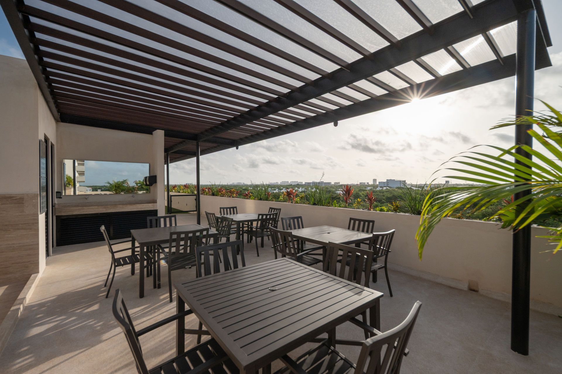 Un patio con mesas y sillas bajo una pérgola.