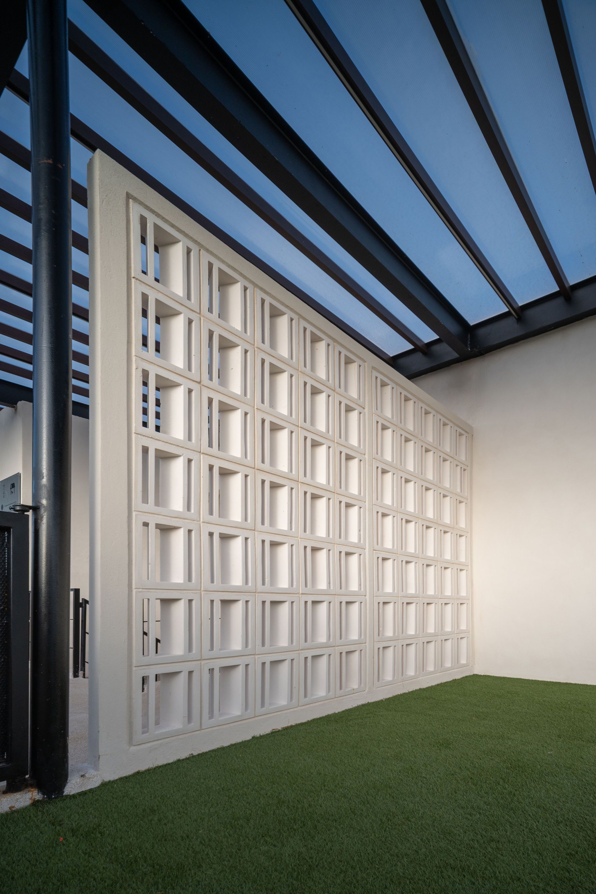 Una pared blanca con muchas ventanas está rodeada de césped y una pérgola.