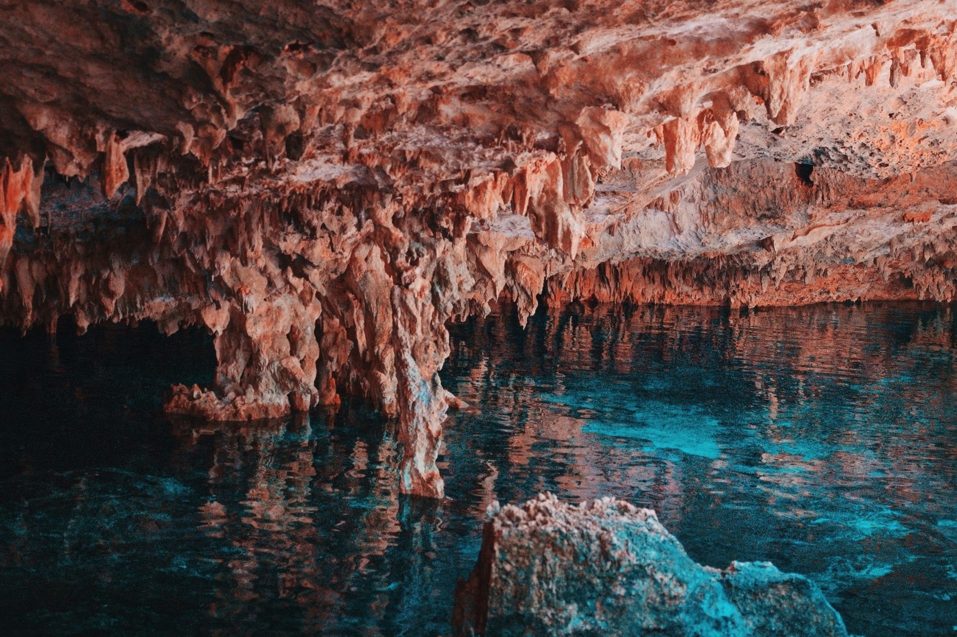 Cueva con agua turquesa que refleja estalactitas y formaciones rocosas.