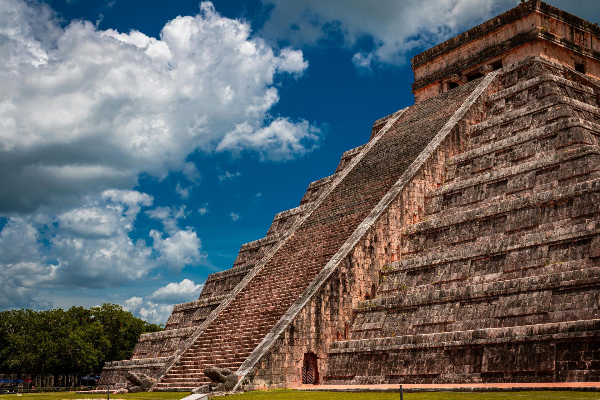 Pirámide de El Castillo en Chichén Itzá, México, estructura de piedra con escaleras, contra un cielo azul con nubes.